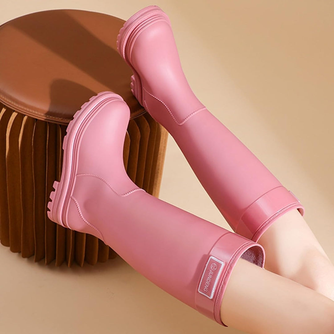 Pink knee high rain boots with side tab, worn in a seated pose
