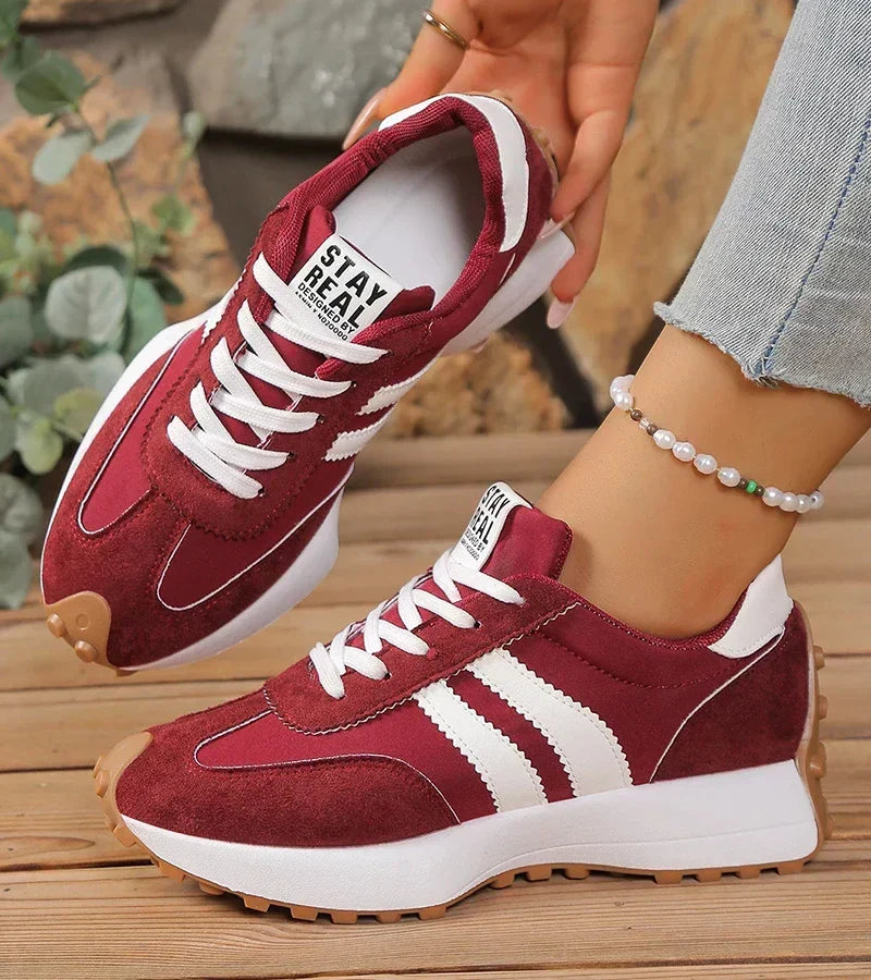 Burgundy striped sneakers with white laces, one shoe held up by hand
