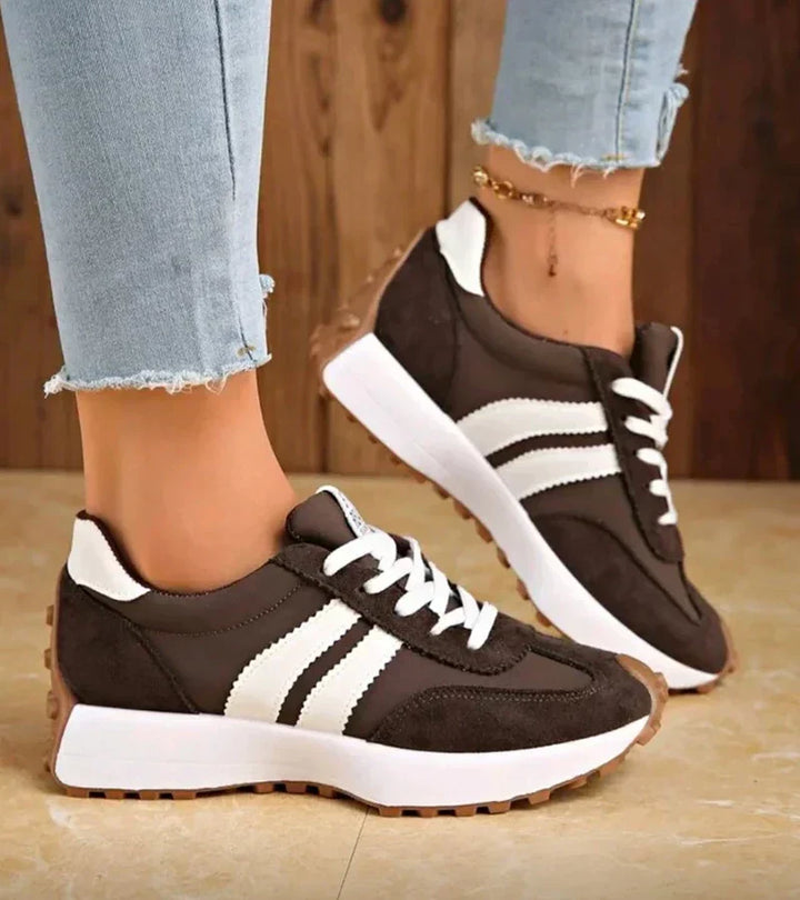 Dark brown low top sneakers with white stripes worn with frayed jeans