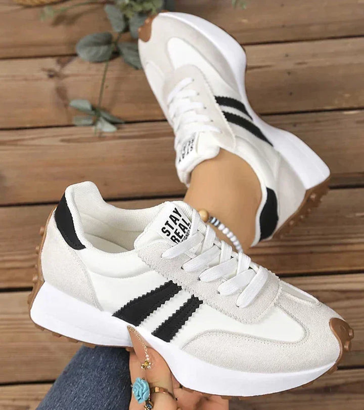 White low top sneakers with black stripes and heel label, worn with jeans
