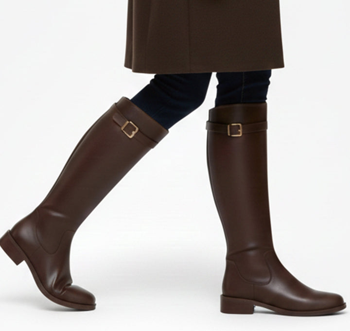 Brown flat riding boots worn over dark denim