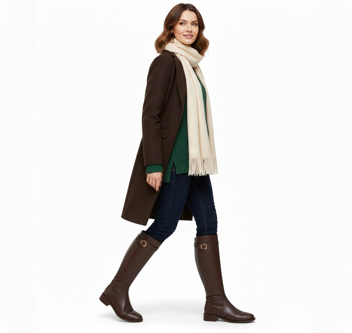 Woman walking in brown riding boots with a long coat and scarf