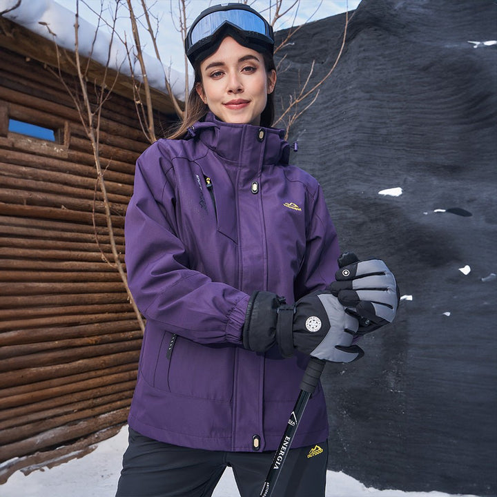 Woman wearing the dark purple ski jacket with goggles outside a log cabin