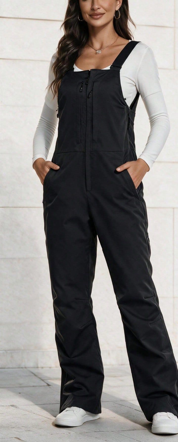 Model wearing the black bib overalls over a white long sleeve top