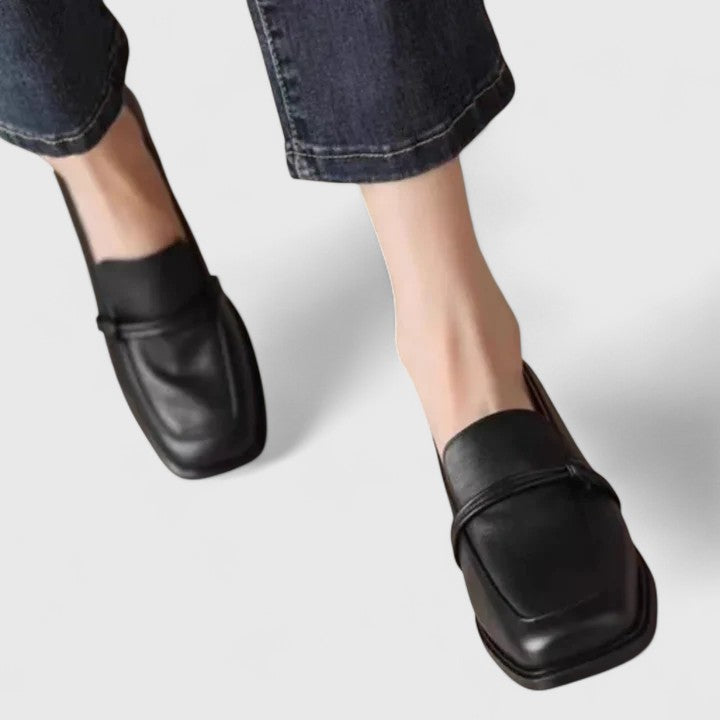 Pair of black square toe loafers worn with cropped dark jeans, front angle