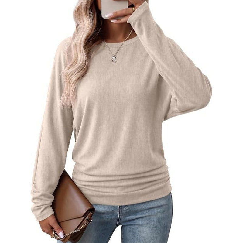 Woman wearing a beige batwing crew neck sweater with ruched hem and jeans