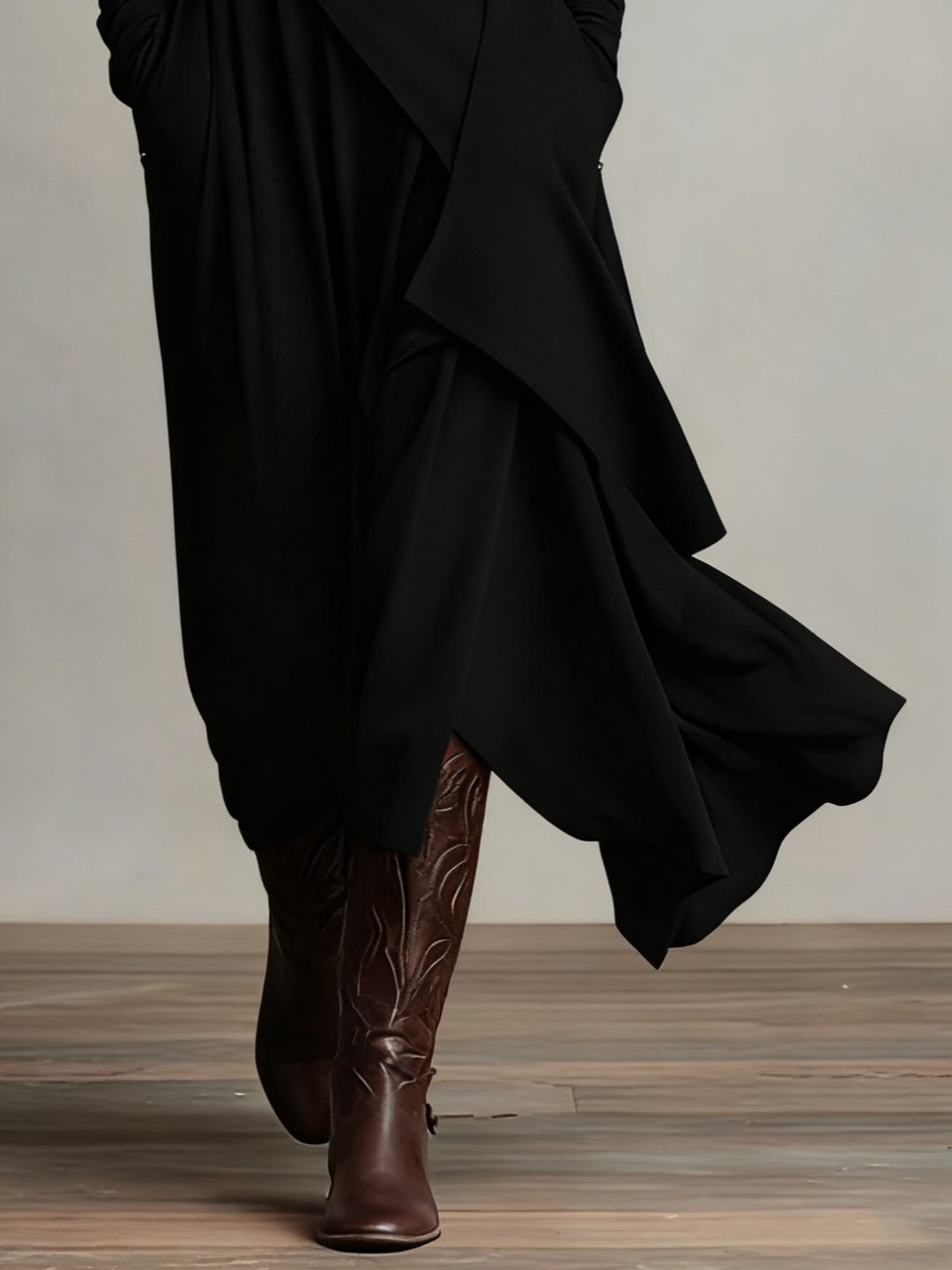 Detail of the black asymmetric hem flowing over brown leather boots