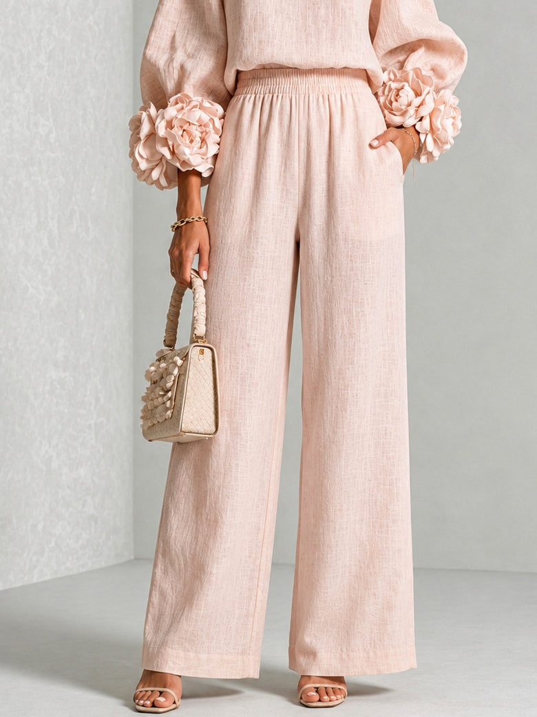 Pink wide leg pants and ruffle cuff knit top, lower body view holding a cream handbag