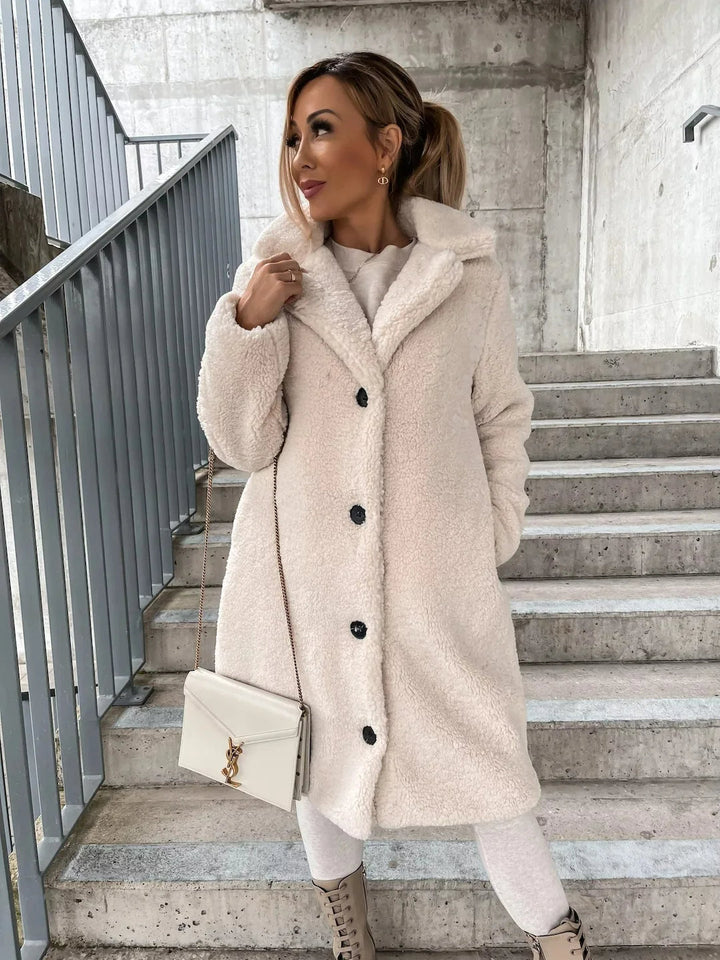 Cream teddy coat with black buttons, model holding a small white handbag