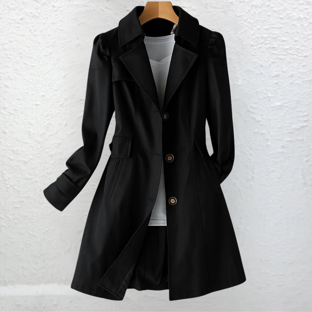 Black trench coat with notch lapels hanging against a white wall