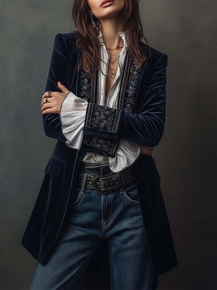 Navy velvet-look long jacket with embroidered lapels, arm crossed over a white blouse