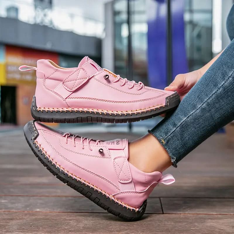 Pink sneakers with strap and laces, held up in hands against a city backdrop