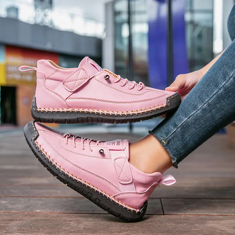 Pink stitched sneakers with strap, held at an angle with jeans in the background