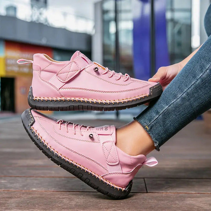 Pink stitched sneakers with strap, held at an angle with jeans in the background