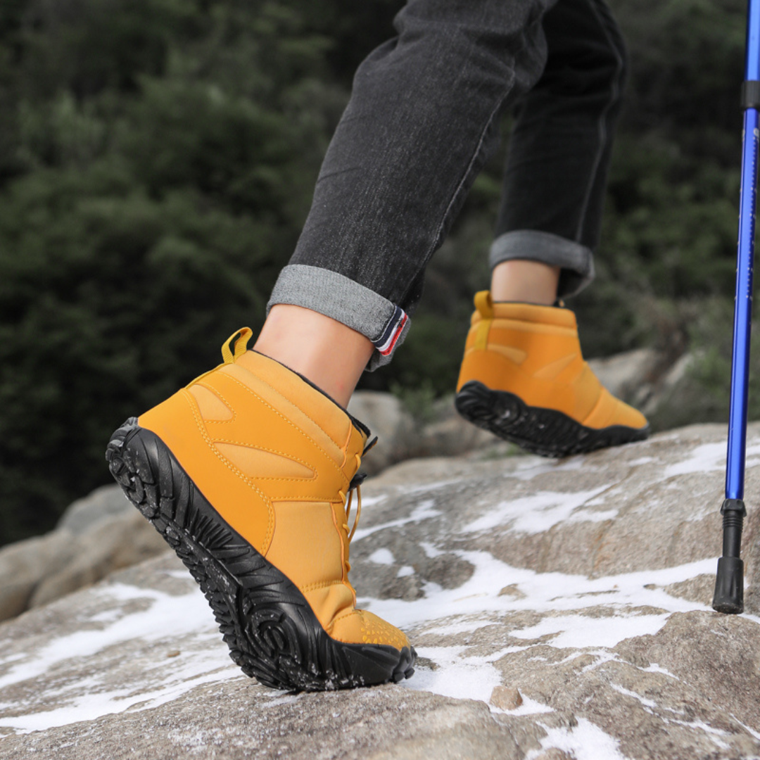 Mustard barefoot style ankle boots worn on rocks with a trekking pole