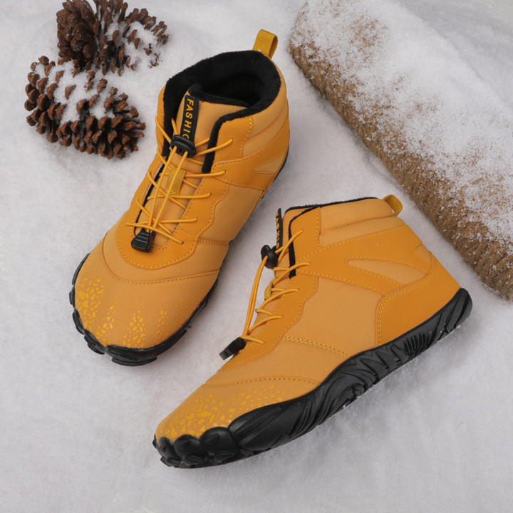 Mustard lace up ankle boots with black flexible soles beside a pine cone