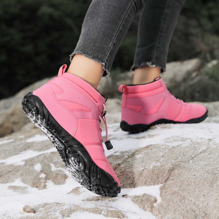 Pink ankle boots with toggle laces worn while hiking on snowy rock
