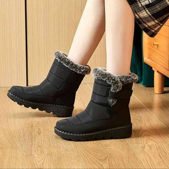 Black ankle boots with faux fur cuff worn seated with crossed legs on a wood floor