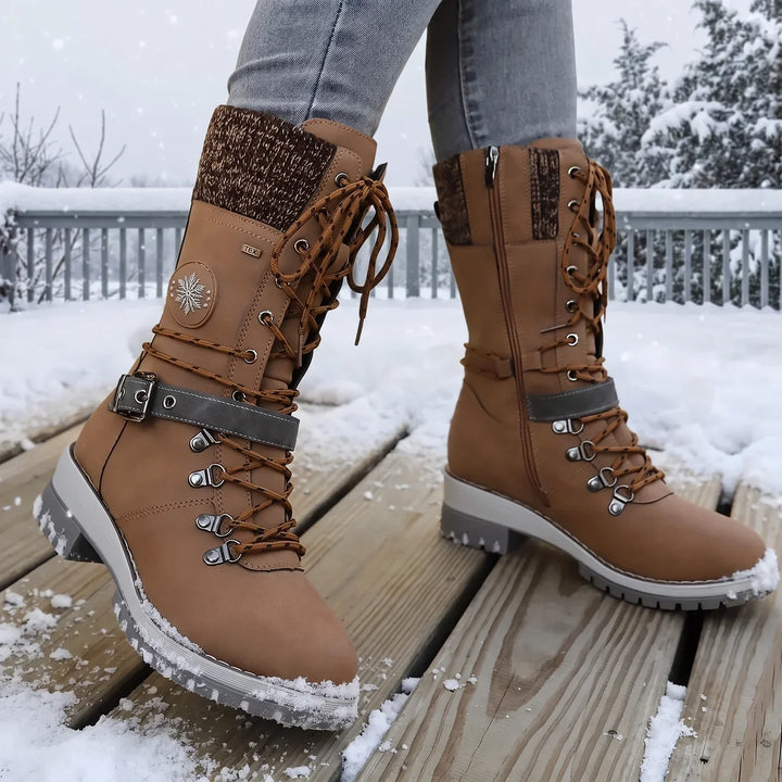 Brown lace up boot with buckle strap worn on a snowy deck with gray jeans