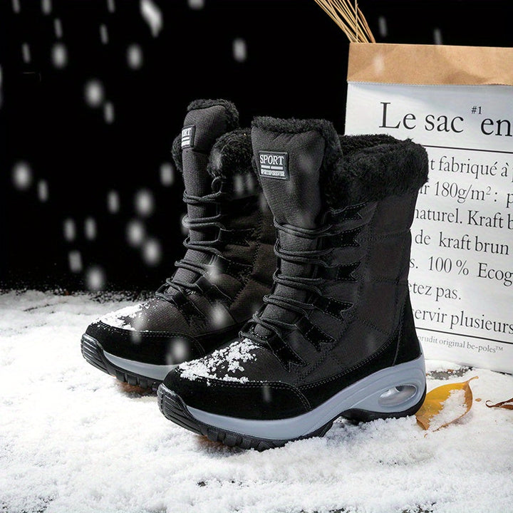 Pair of black lace up boots standing in the snow beside a paper bag
