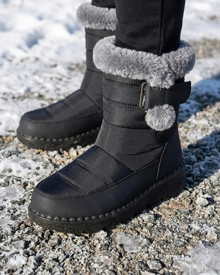 Black boots with faux fur cuffs worn over dark pants on a gravel path