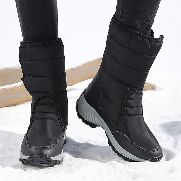 Close-up of black quilted mid calf boots on snow, front view