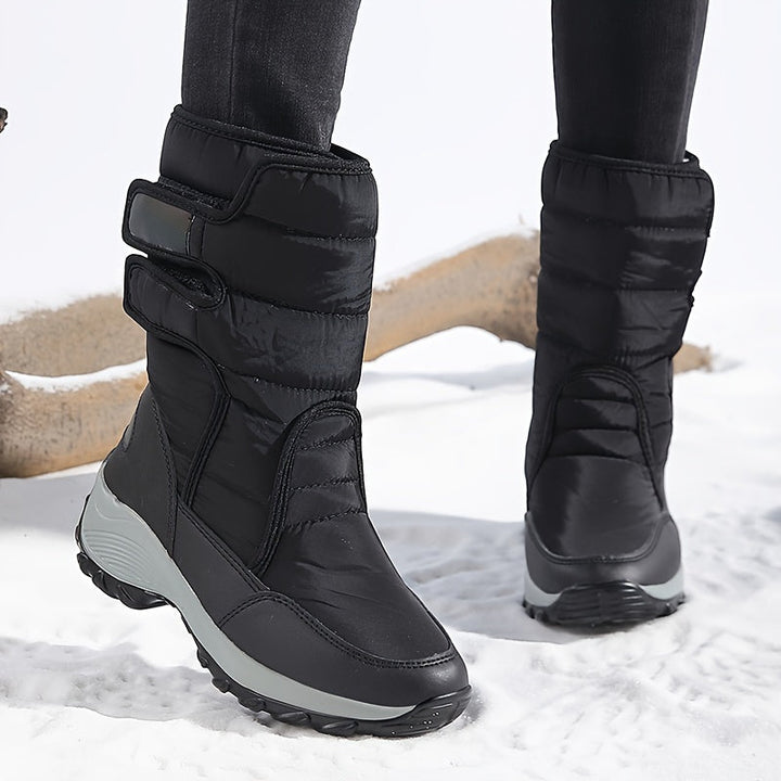Black mid calf boots with double straps and gray sole on snowy ground
