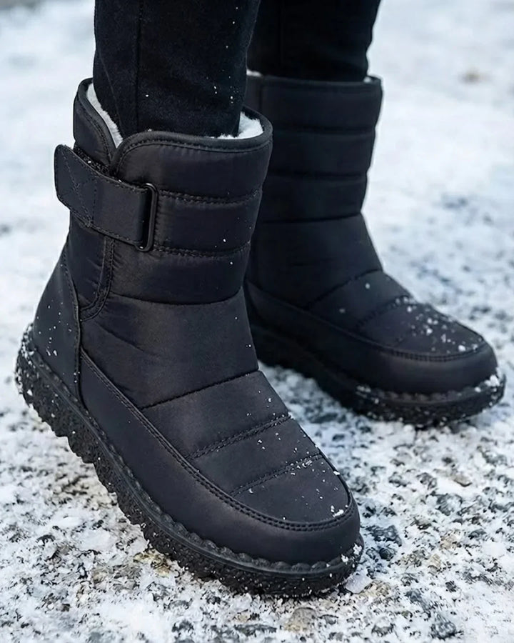 Black quilted mid calf boots worn on a snowy ground, close view
