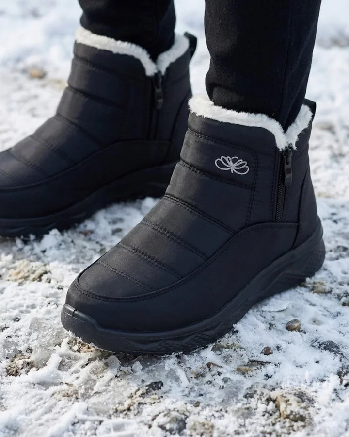 Black quilted ankle boots on snowy ground, close-up of the side zip