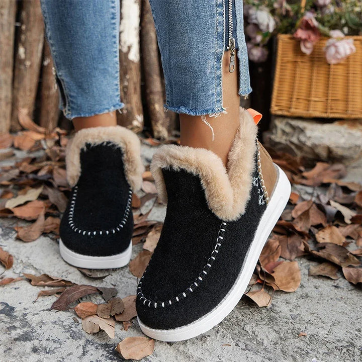 Black slip on ankle boots with faux fur trim worn with cuffed jeans on leaves