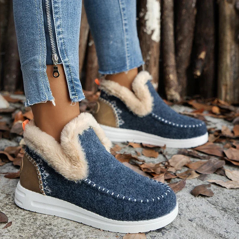 Navy fur-trimmed slip on boots with white sole, side view against wood posts