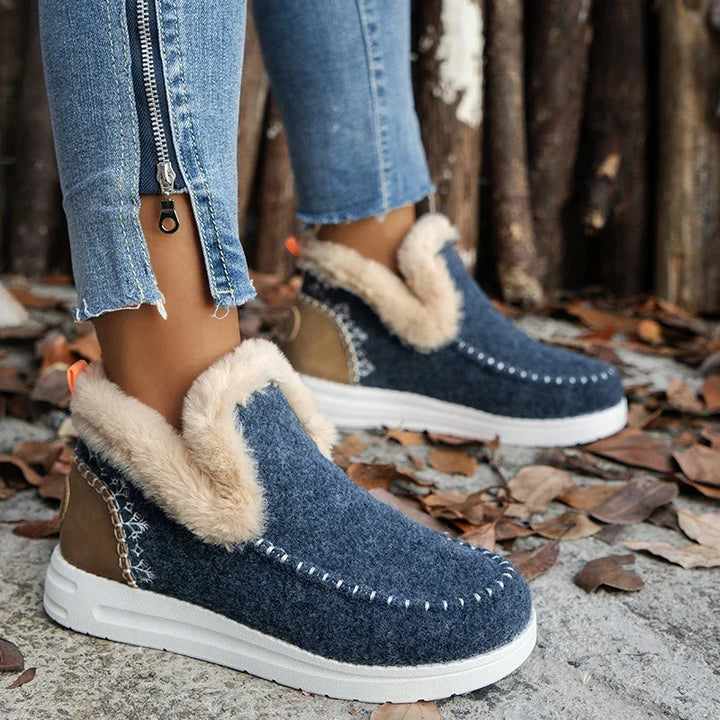 Navy fur-trimmed slip on boots with white sole, side view against wood posts