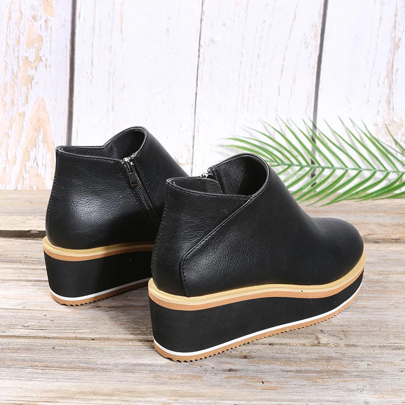 Black platform wedge ankle boots with side zip seen from behind on a wooden table