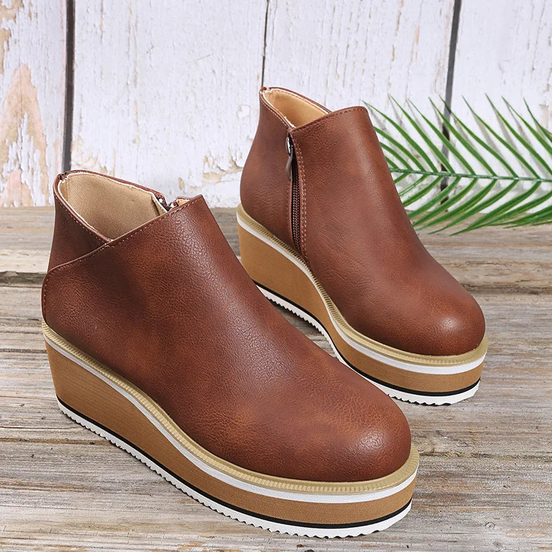 Brown platform wedge booties with side zip on a wooden table with a palm leaf