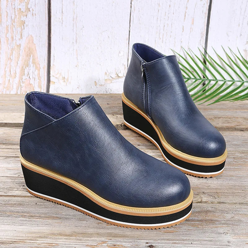 Navy platform wedge booties with a black sole and tan stripe on a wooden table