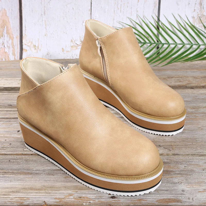 Tan platform wedge booties with side zip and layered sole on a wooden table