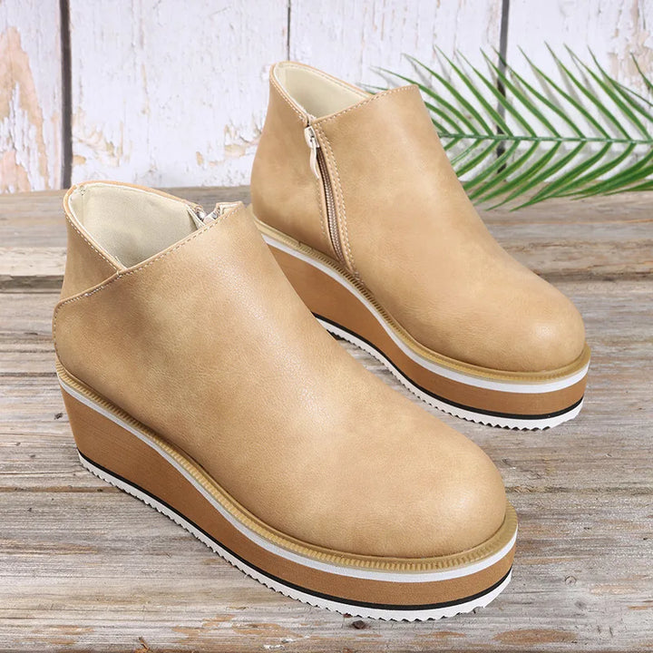 Tan platform wedge booties with side zip and layered sole on a wooden table
