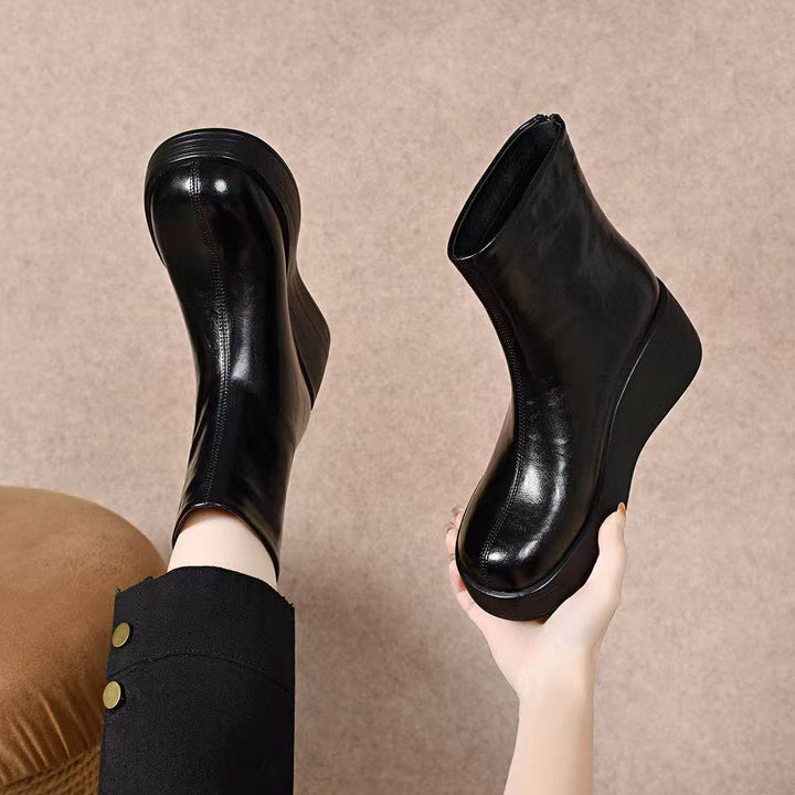 Black wedge ankle booties held in a hand, back zip and platform sole visible