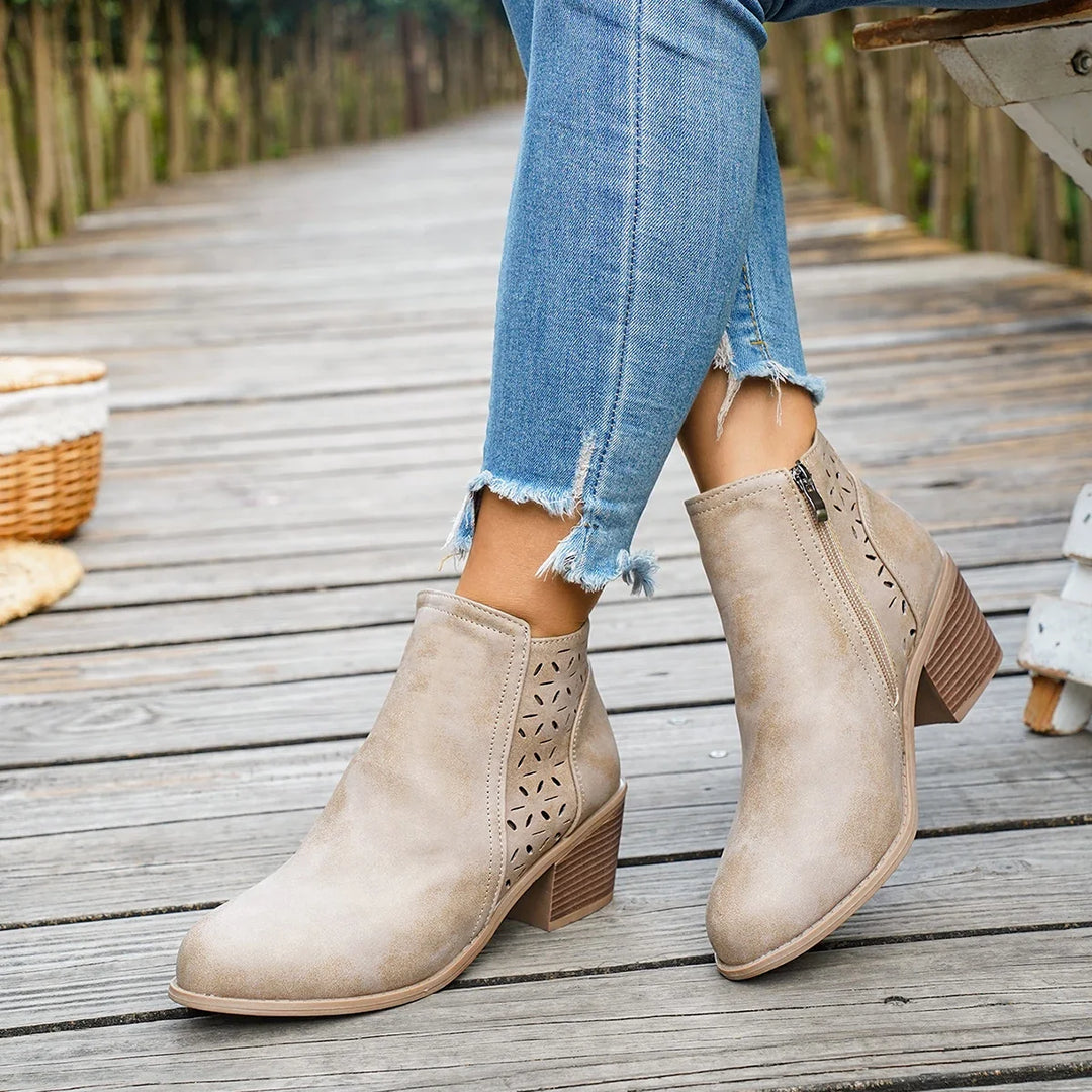 Beige perforated block heel booties worn with cuffed jeans on a wooden path