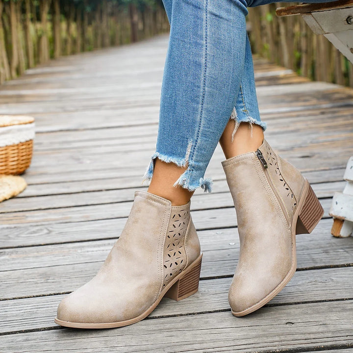 Beige perforated block heel booties worn with cuffed jeans on a wooden path