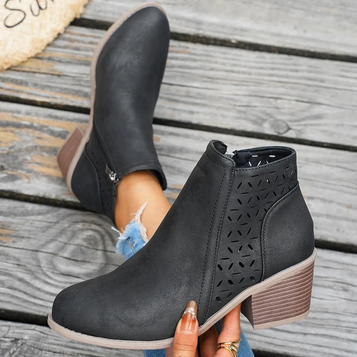 Black perforated western ankle boot held in a hand, showing the side zip and block heel