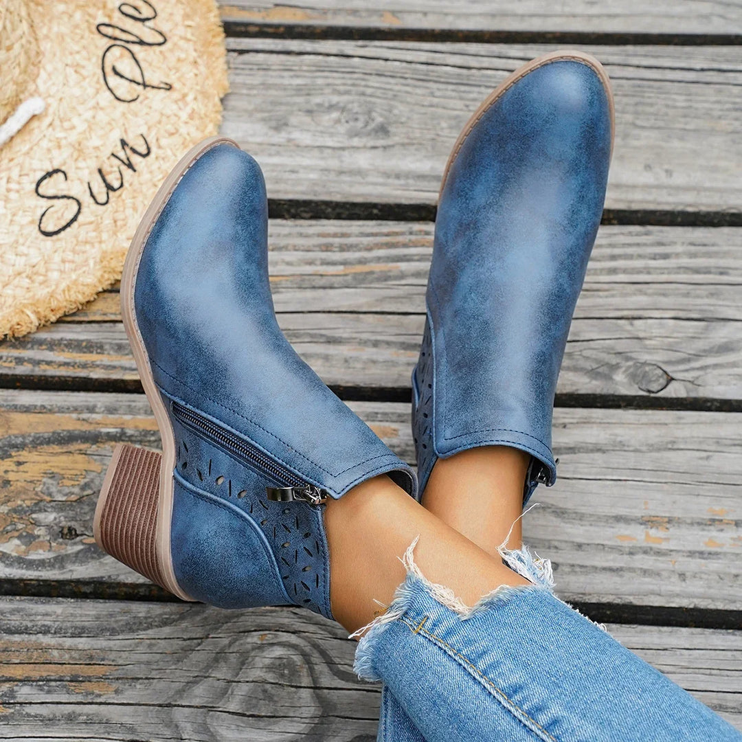 Blue western ankle boots with block heel worn with jeans, feet raised on a wooden surface