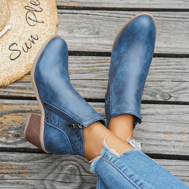 Blue western ankle boots with block heel worn with jeans, feet raised on a wooden surface