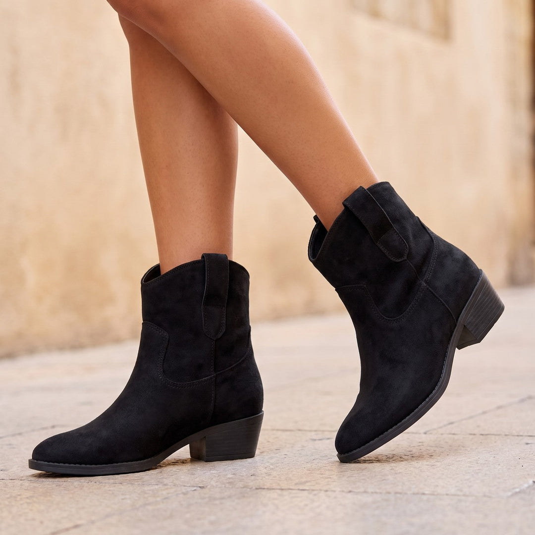 Black short cowboy boots with a low stacked heel worn on a stone path