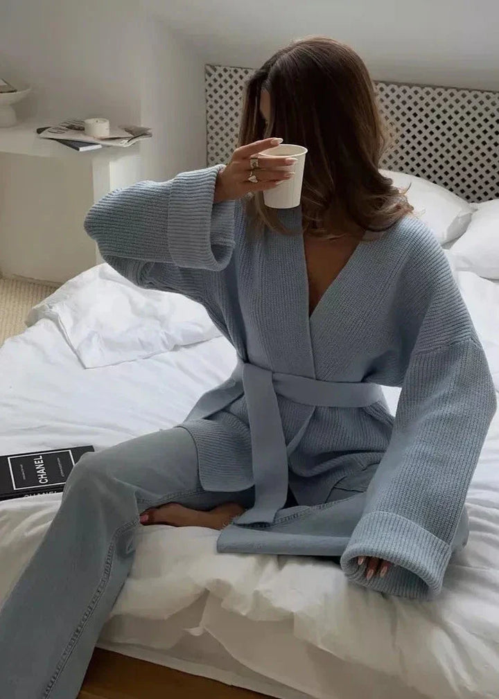 Woman relaxing on a bed in the light blue belted sweater coat