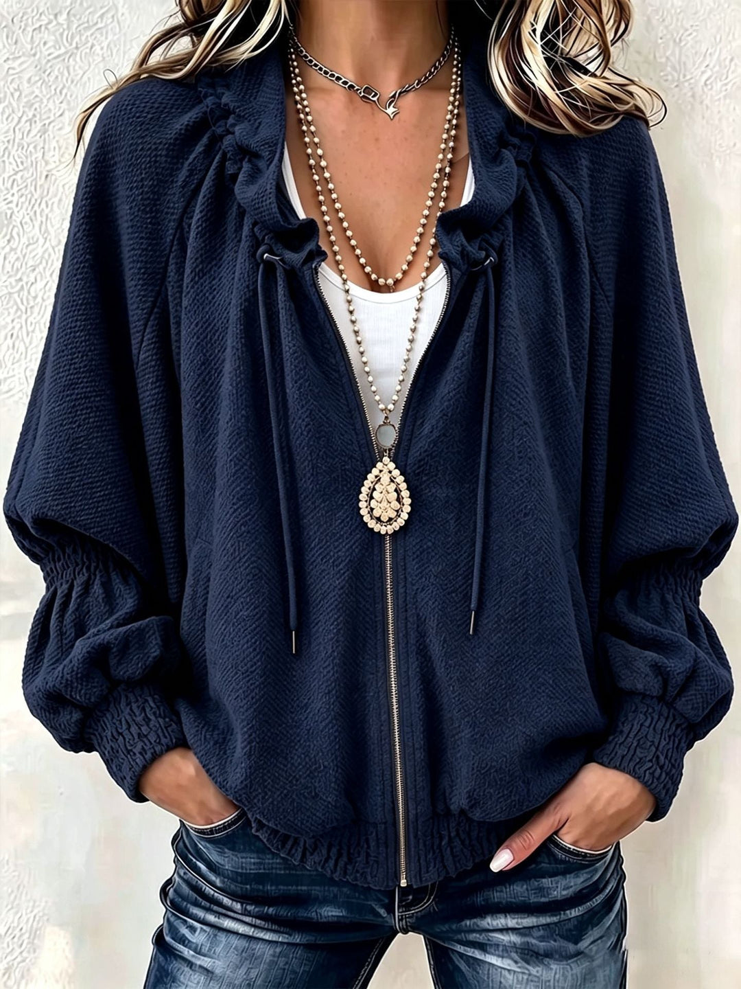 Navy textured jacket worn open over a white tank with a long pendant necklace